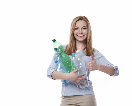 A young woman with shoulder-length blonde hair, wearing a light grey long-sleeved top and beige trousers, is standing against a white background. She is holding several transparent plastic bottles of varying sizes, some with green or blue caps, pressed against her chest. The bottles appear to be empty and are made of clear plastic with visible ridges and labels. The woman is smiling broadly and giving a thumbs-up with her right hand, conveying a positive attitude toward recycling or waste disposal. The image's clean background and her casual attire suggest a context related to rubbish or waste management, aligning with services offered by Garden Clearance Holborn. This visual emphasizes environmentally conscious rubbish collection, particularly the removal and recycling of plastic waste, relevant to green disposal initiatives in the local area.